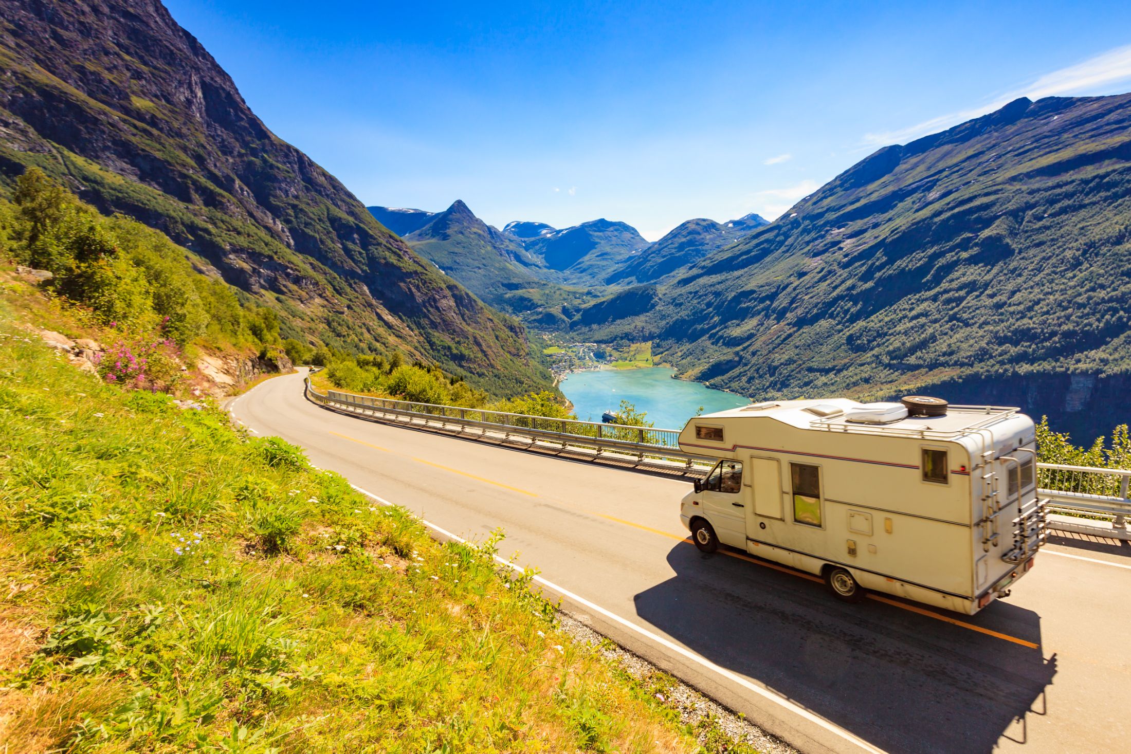 RV camper parked on mountain road overlooking turquoise alpine lake and valley