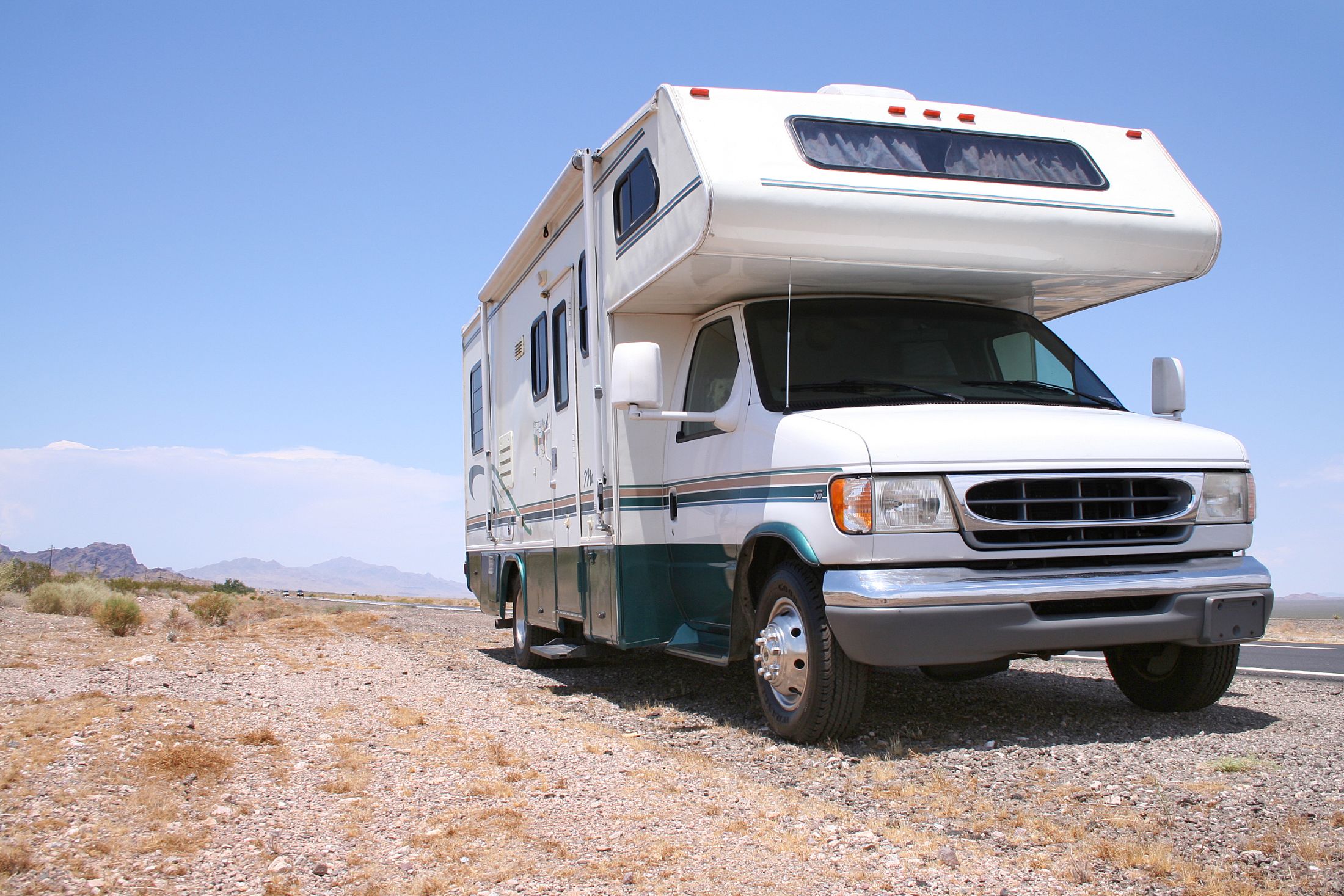 White and green camper van parked on desert terrain with mountains in background
